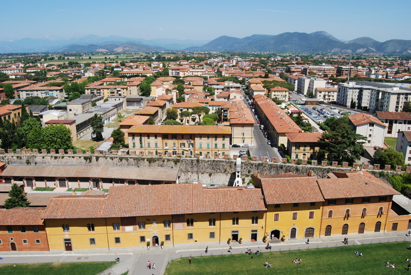 16 - High-angle view looks north from the Leaning Tower of Pisa across the historic rooftops of Pisa, Italy, capturing the urban layout and the surrounding Tuscan landscape